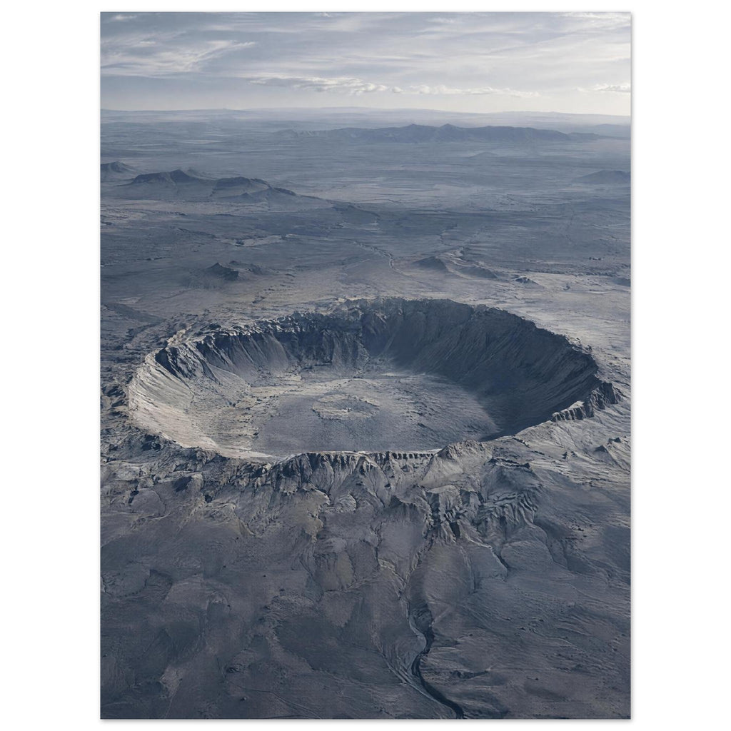Large circular crater in a blue-grey desert plain, with rugged slopes, distant hills and a cloudy sky.