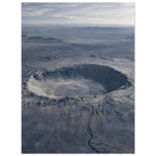 Large circular crater in a blue-grey desert plain, with rugged slopes, distant hills and a cloudy sky.