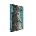 Tall, craggy grey rock stack on a rocky shore, with waves behind it and a teal sky under a distressed texture.