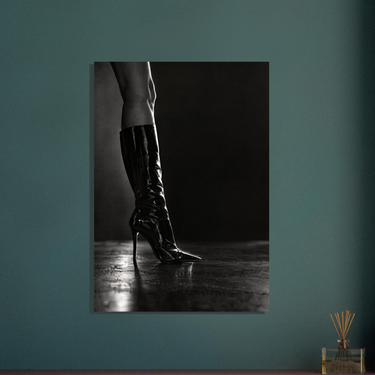 Black and white photograph of a leg in a glossy knee-high stiletto boot on a reflective floor against a dark backdrop.