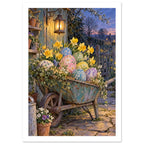 Wheelbarrow filled with patterned Easter eggs, daffodils and trailing flowers beside a glowing lantern at dusk.