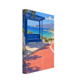 Blue bus shelter beside a coral road overlooking a turquoise bay, sandy beach, white buildings and distant mountains.