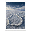 Salt flats with raised polygon-shaped ridges stretching towards distant mountains beneath a blue, cloud-streaked sky.