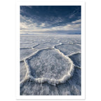 Salt flats with raised polygon-shaped ridges stretching towards distant mountains beneath a blue, cloud-streaked sky.
