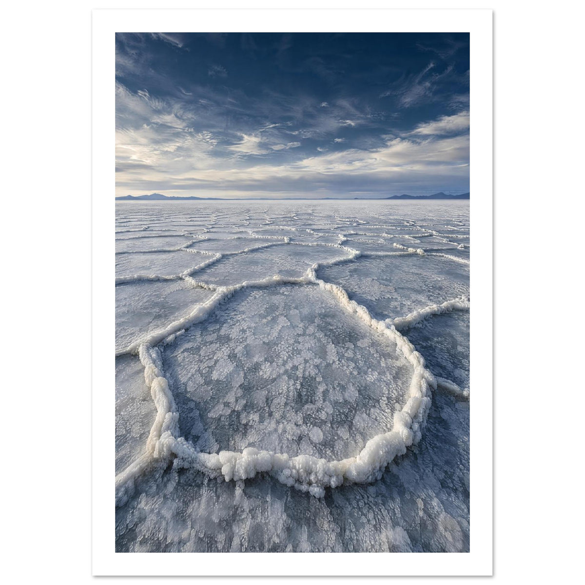 Salt flats with raised polygon-shaped ridges stretching towards distant mountains beneath a blue, cloud-streaked sky.