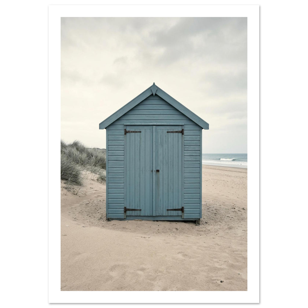Blue wooden beach hut with closed doors on pale sand, with dune grasses, sea waves and an overcast sky.