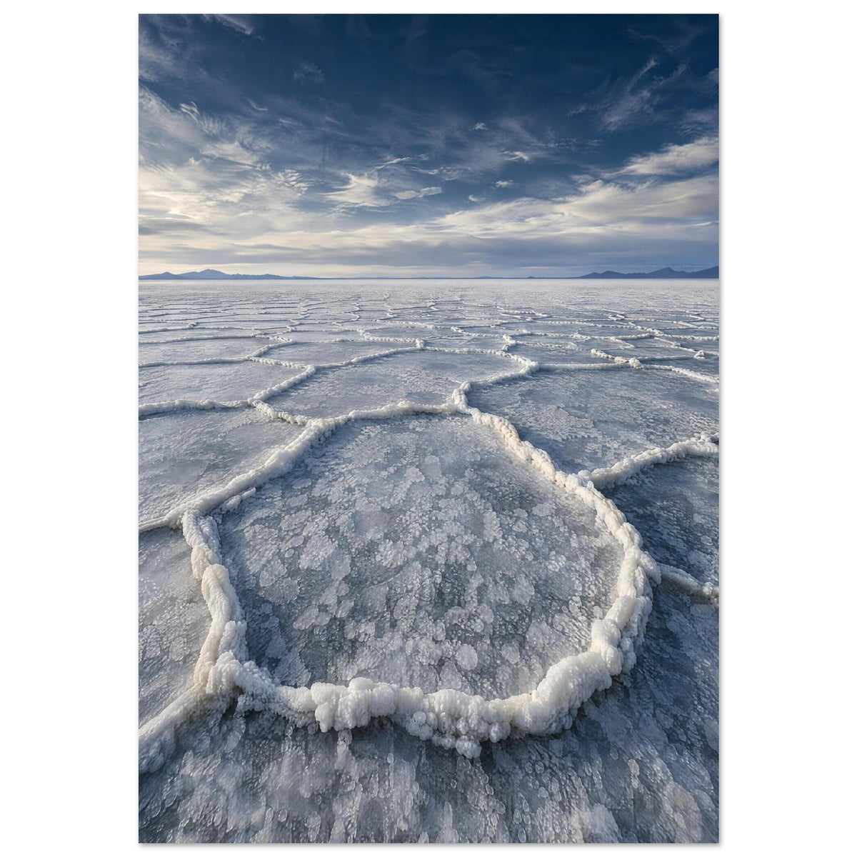 Salt flats with raised polygon-shaped ridges stretching towards distant mountains beneath a blue, cloud-streaked sky.