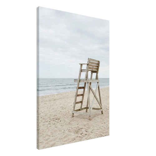 Empty wooden lifeguard chair on pale sand beside gentle sea waves beneath an overcast sky.