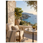 Lemon tree on a stone terrace with a cushioned chair, round table and blue sea overlooking a rocky coastline.