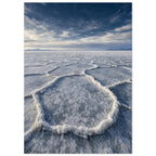Salt flats with raised polygon-shaped ridges stretching towards distant mountains beneath a blue, cloud-streaked sky.