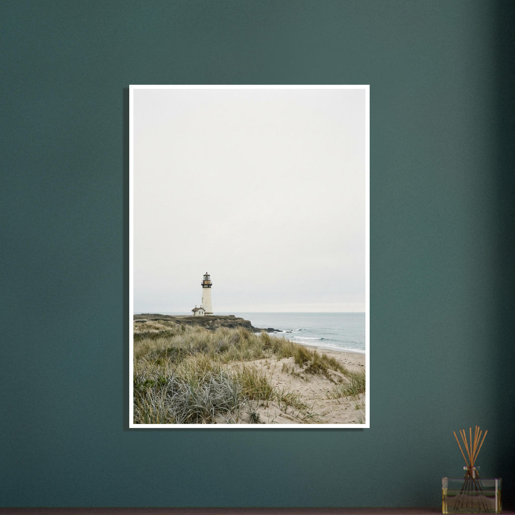 Lighthouse on a rocky headland beyond grassy sand dunes, with gentle waves and a wide, pale grey sky.
