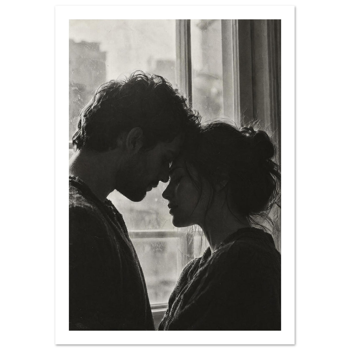 Black and white photograph of a couple touching foreheads beside a window, their profiles softly outlined by daylight.