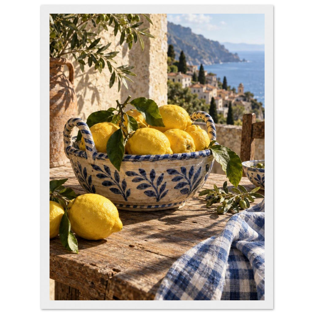 Lemons in a blue-and-white bowl on a wooden table, with olive branches, checked cloth and a coastal village beyond.
