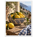 Lemons in a blue-and-white bowl on a wooden table, with olive branches, checked cloth and a coastal village beyond.