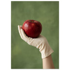 Red apple resting in a cream-gloved hand, with a bare forearm below and a softly blurred green background.