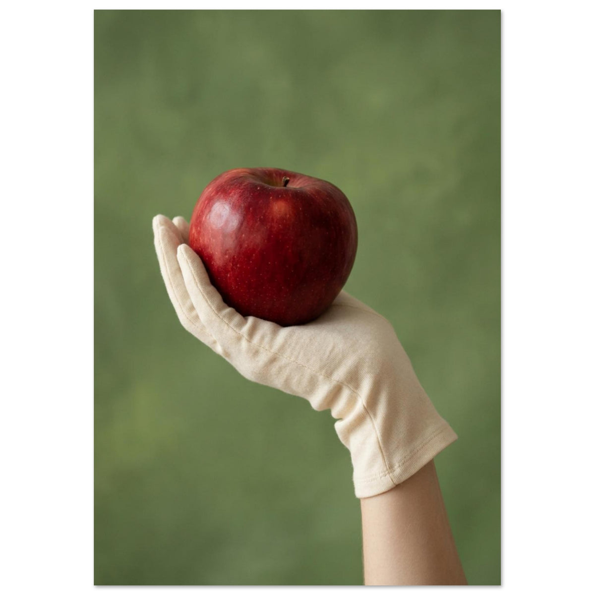 Red apple resting in a cream-gloved hand, with a bare forearm below and a softly blurred green background.