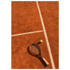 Tennis racket and yellow-green ball on an orange clay court, with white lines, footprints and strong shadows.