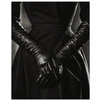 Overlapping hands in long black leather gloves against a dark fitted outfit, photographed in black and white.