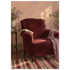 The Reading Chair painting showing a burgundy armchair with an open book, a cropped striped rug and afternoon light.