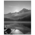 Mountain peaks and conifer forests reflected in a misty lake, with rocks in the foreground, in black and white.
