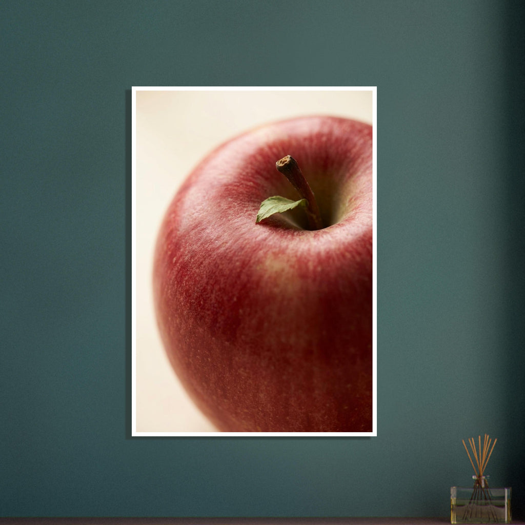 Close-up of a red apple with mottled skin, a brown stalk and a small green leaf against a soft cream background.