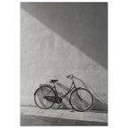 Bicycle leaning against a textured wall, with diagonal sunlight and long shadows across the wall and pavement.