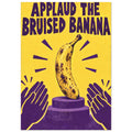 Bruised banana on a purple podium with clapping hands, a yellow background and the words ‘Applaud the Bruised Banana’.