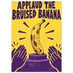 Bruised banana on a purple podium with clapping hands, a yellow background and the words ‘Applaud the Bruised Banana’.