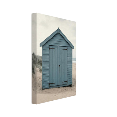 Blue wooden beach hut with closed doors on pale sand, with dune grasses, sea waves and an overcast sky.