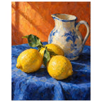 Three yellow lemons with green leaves beside a cream and blue floral jug on blue cloth against an orange background.