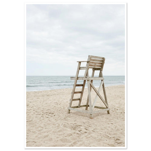 Empty wooden lifeguard chair on pale sand beside gentle sea waves beneath an overcast sky.