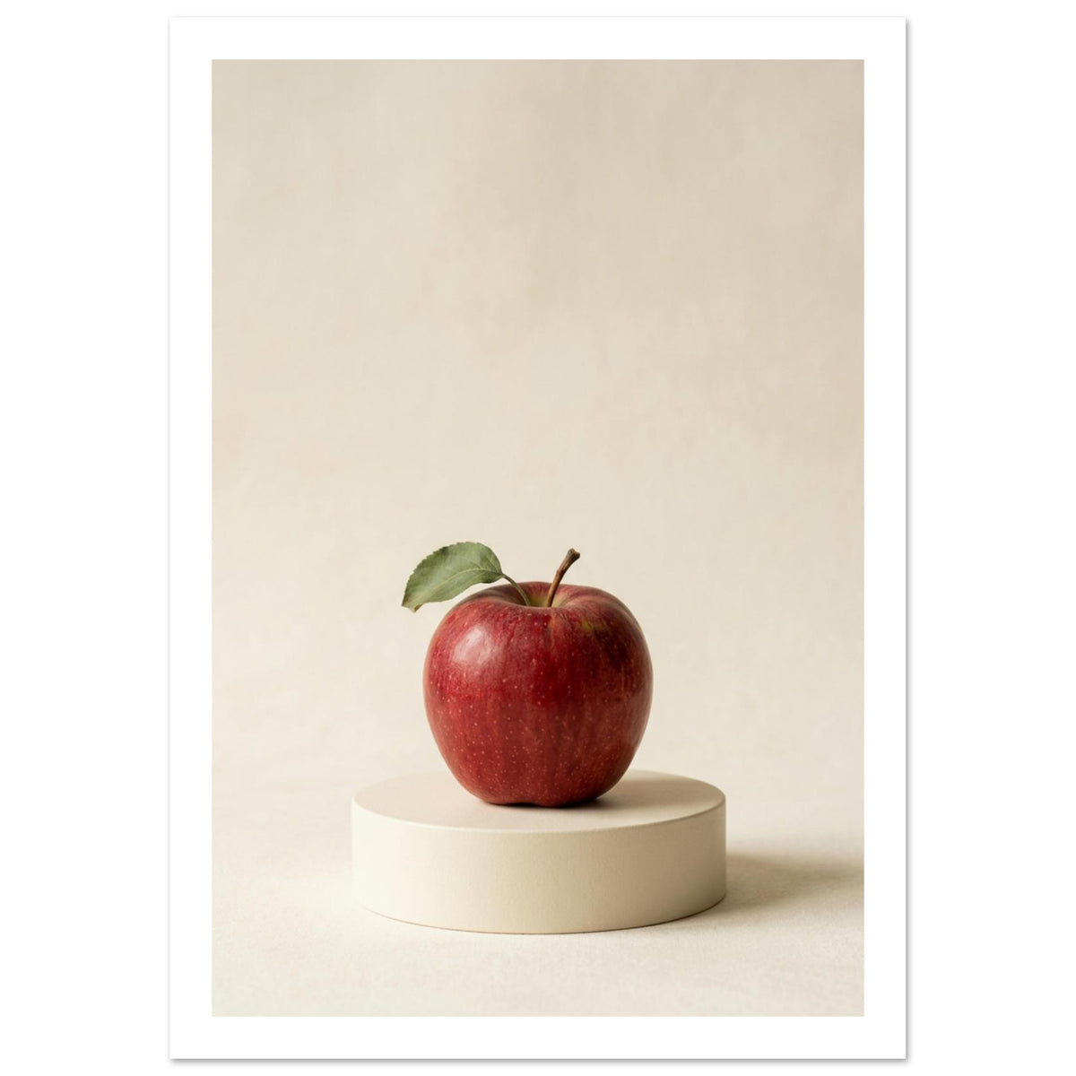 Red apple with a green leaf on a low circular cream plinth, against a cream background with soft shadows.