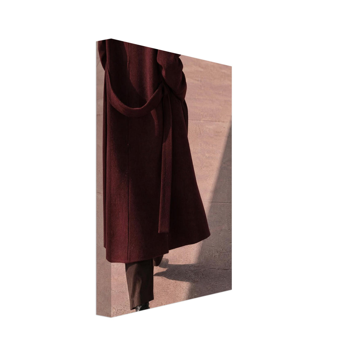 Figure seen from behind in a long burgundy coat, brown trousers and black boots on pink pavement with diagonal shadows.