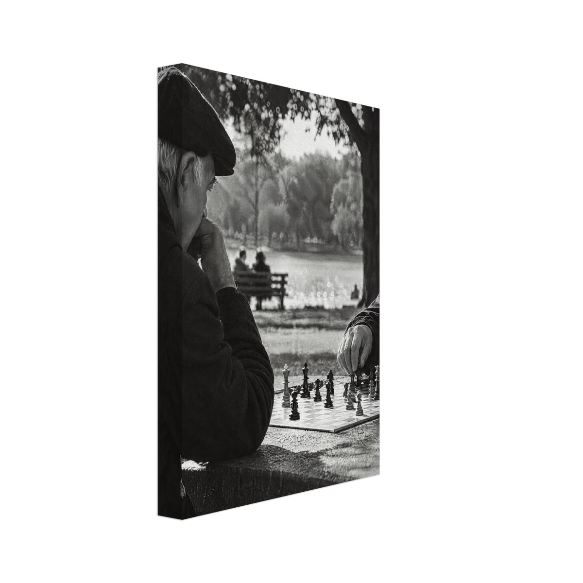 Two men in flat caps playing chess at a stone table beside water and trees, photographed in black and white.