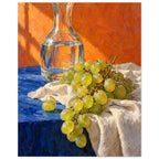 Green grapes on cream fabric beside a glass carafe of water, with a blue tabletop and textured orange background.