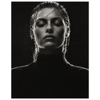 Black and white portrait of a woman with closed eyes, slicked-back hair and a dark high-neck top against black.