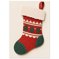 Red Christmas stocking with green trees, heel and toe, cream decorative trim and a paper-cut texture on a cream background.