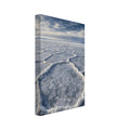 Salt flats with raised polygon-shaped ridges stretching towards distant mountains beneath a blue, cloud-streaked sky.