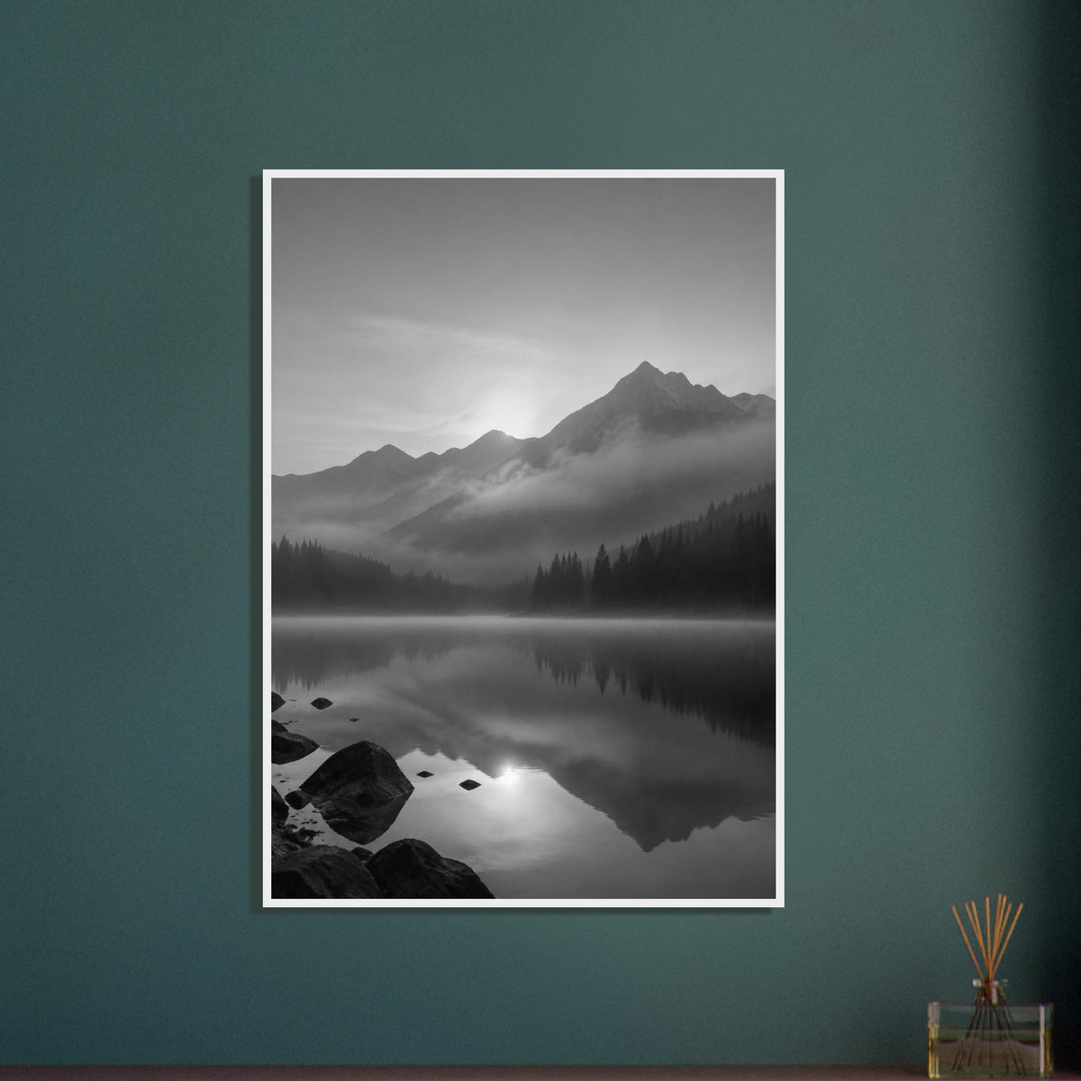 Mountain peaks and conifer forests reflected in a misty lake, with rocks in the foreground, in black and white.