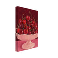Red and burgundy cherries in a pale pink pedestal bowl on a pink tabletop against a deep red painted background.