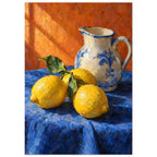 Three yellow lemons with green leaves beside a cream and blue floral jug on blue cloth against an orange background.