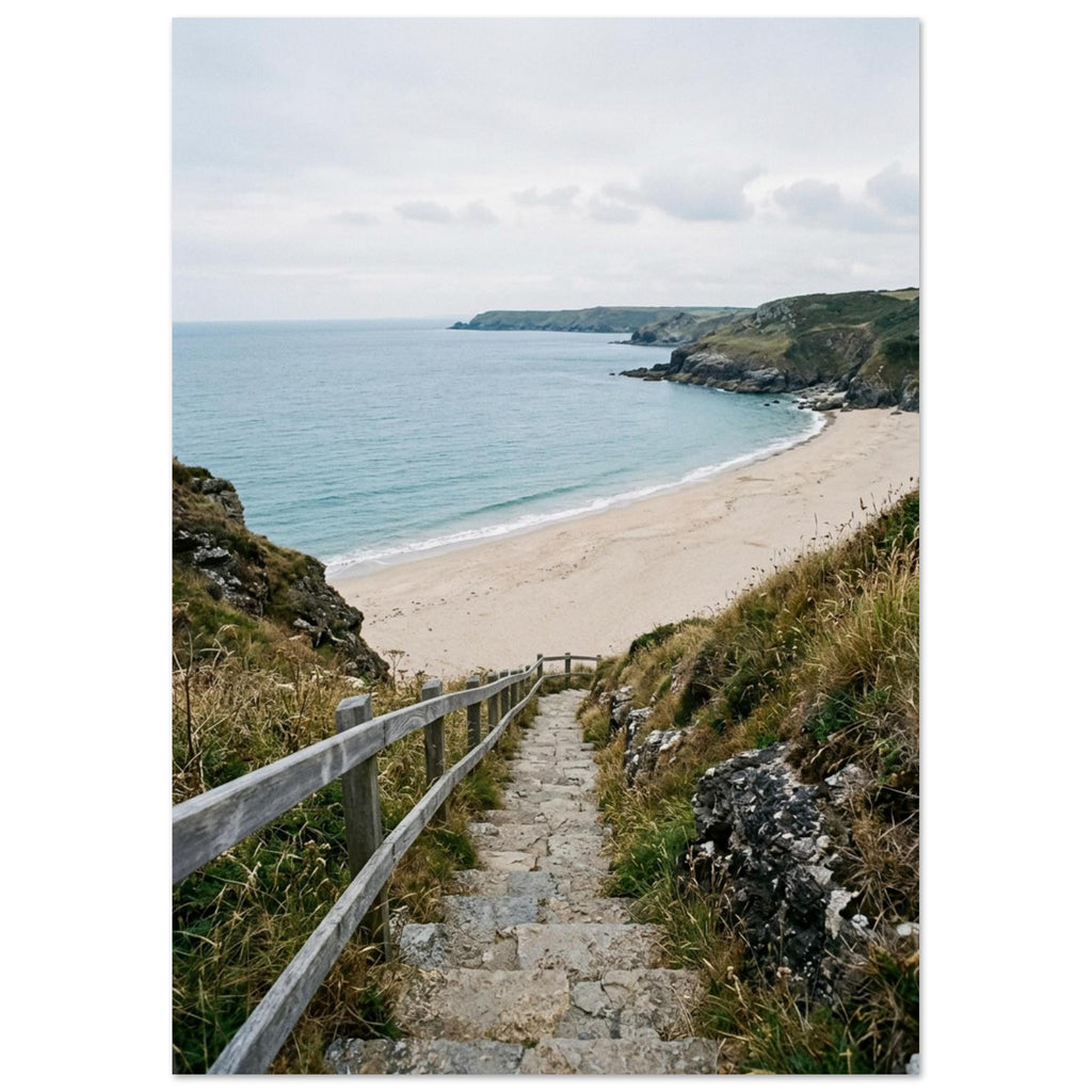 Stone steps with a wooden handrail descend through coastal grasses to a sandy beach, blue sea and rocky headlands.