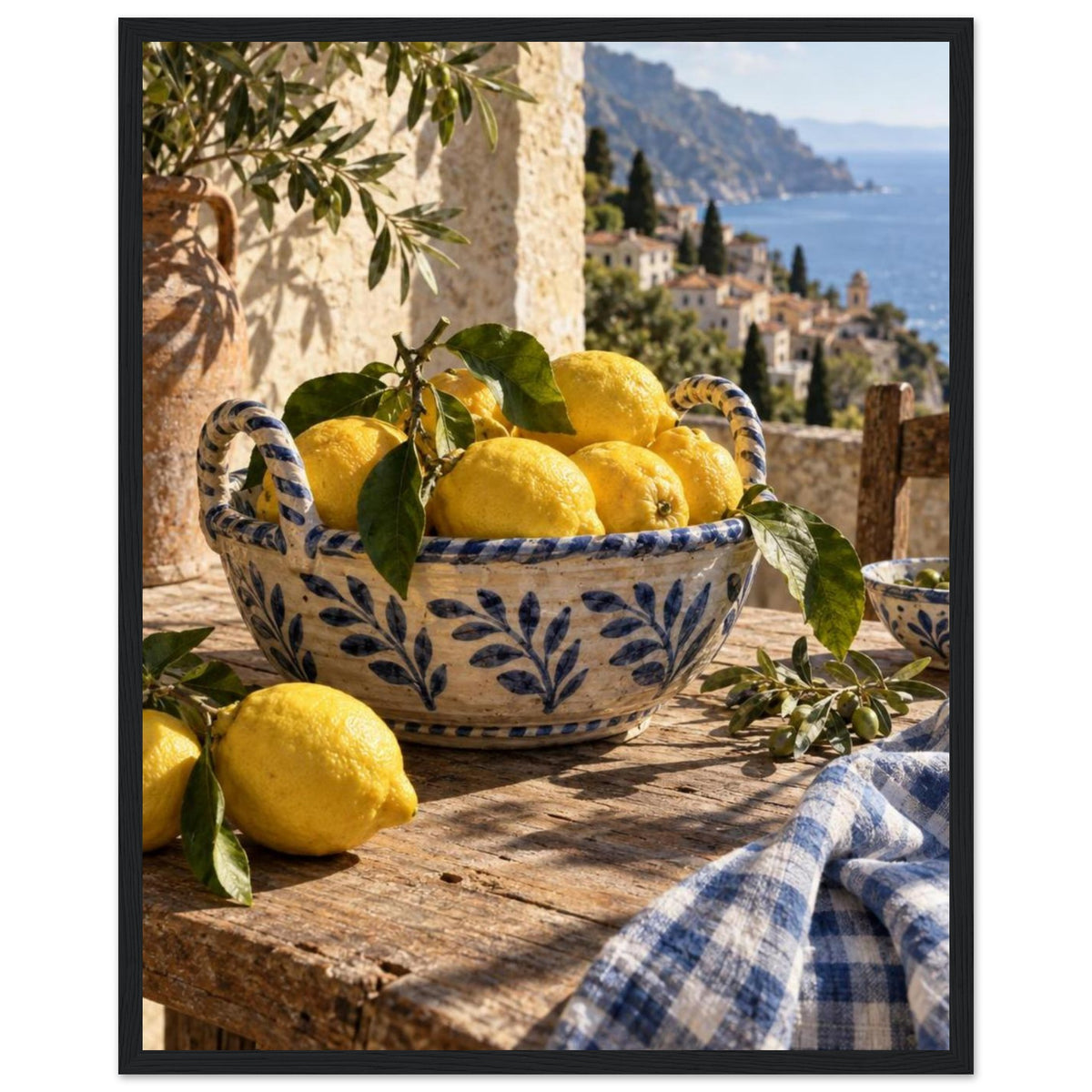 Lemons in a blue-and-white bowl on a wooden table, with olive branches, checked cloth and a coastal village beyond.