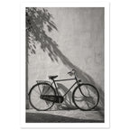 Bicycle leaning against a textured wall with long leafy shadows above and stone paving below, in black and white.
