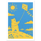 Yellow bear flying a kite beneath a sun and clouds, beside blue water with tree-lined banks, in a paper-cut style.
