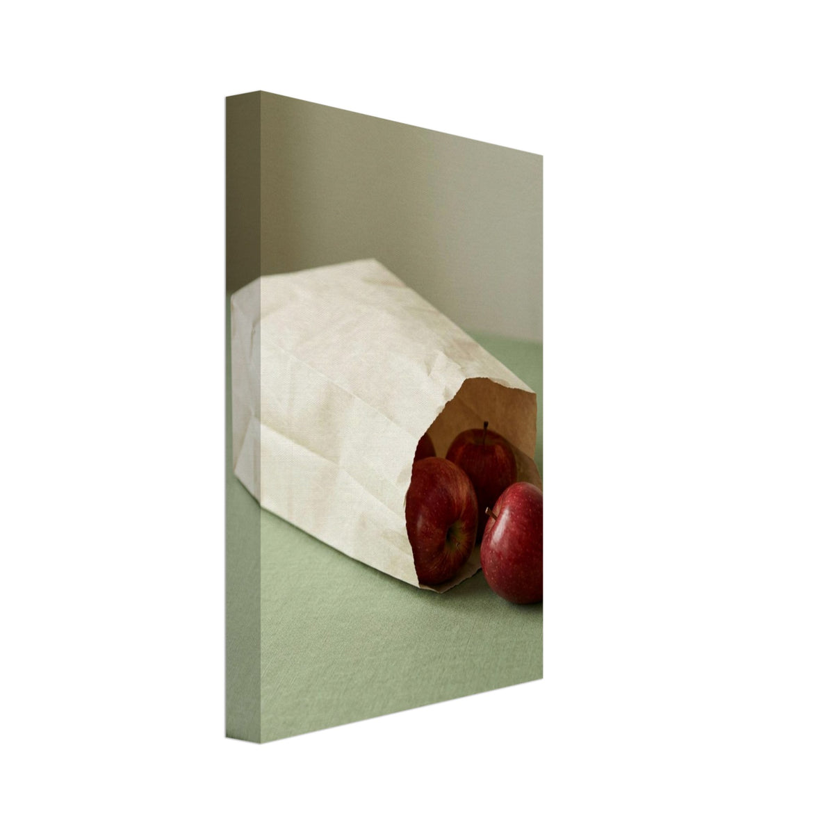 Red apples spilling from a cream paper bag lying on its side on a sage-green tablecloth against a muted background.