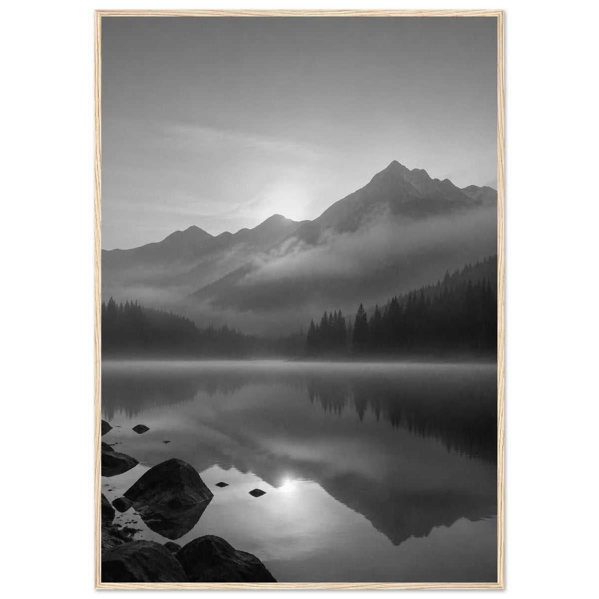 Mountain peaks and conifer forests reflected in a misty lake, with rocks in the foreground, in black and white.