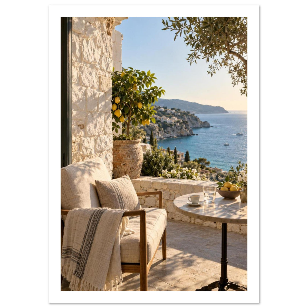 Sunlit stone terrace with a cushioned chair, round table and potted lemon tree overlooking blue sea and cliffs.