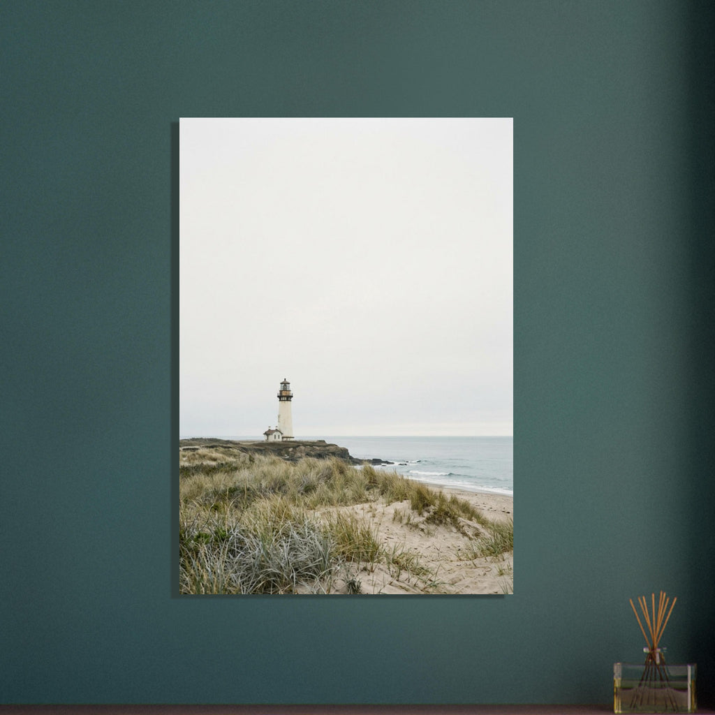 Lighthouse on a rocky headland beyond grassy sand dunes, with gentle waves and a wide, pale grey sky.
