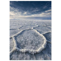 Salt flats with raised polygon-shaped ridges stretching towards distant mountains beneath a blue, cloud-streaked sky.
